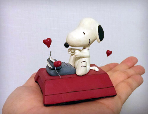 Snoopy from The Peanuts siting on his red dog house typing on little typewriter statue by Marten Go aka MGO in his palm