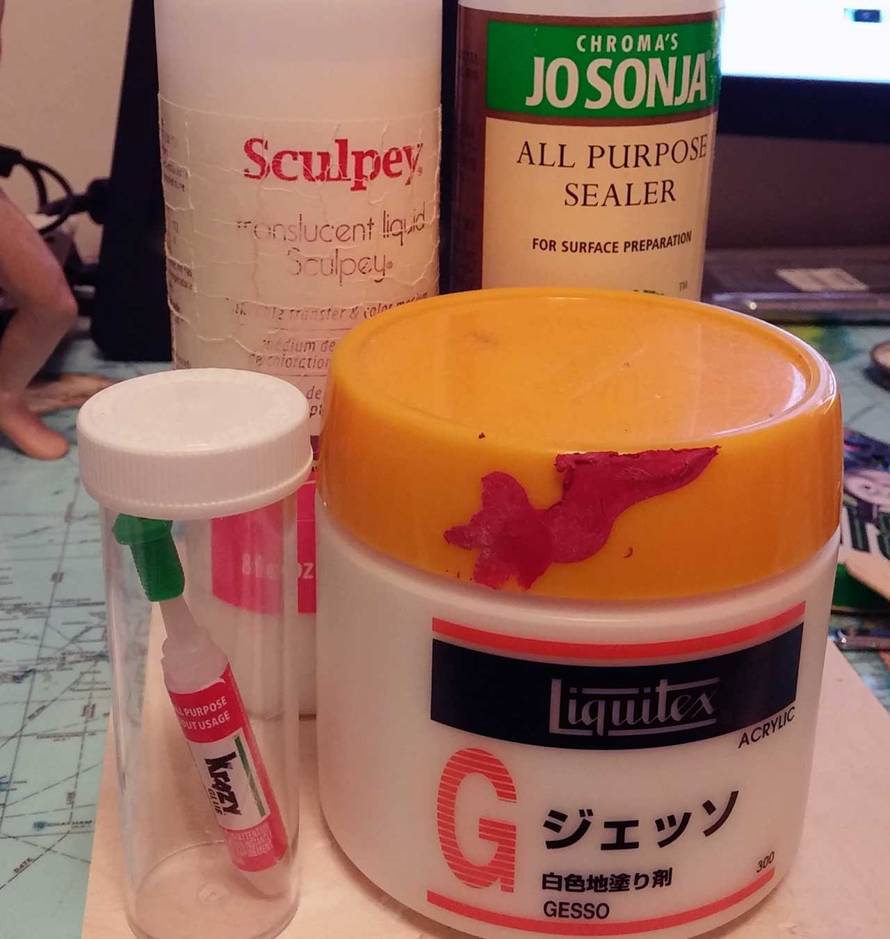 Liquitex Gesso, Krazy glue, Jo Sonja All Purpose Sealer and Sculpey translucent liquid on desk